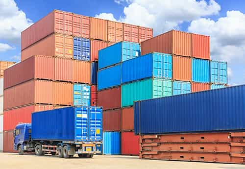 shipping containers stacked in storage yard with a semi truck driving away